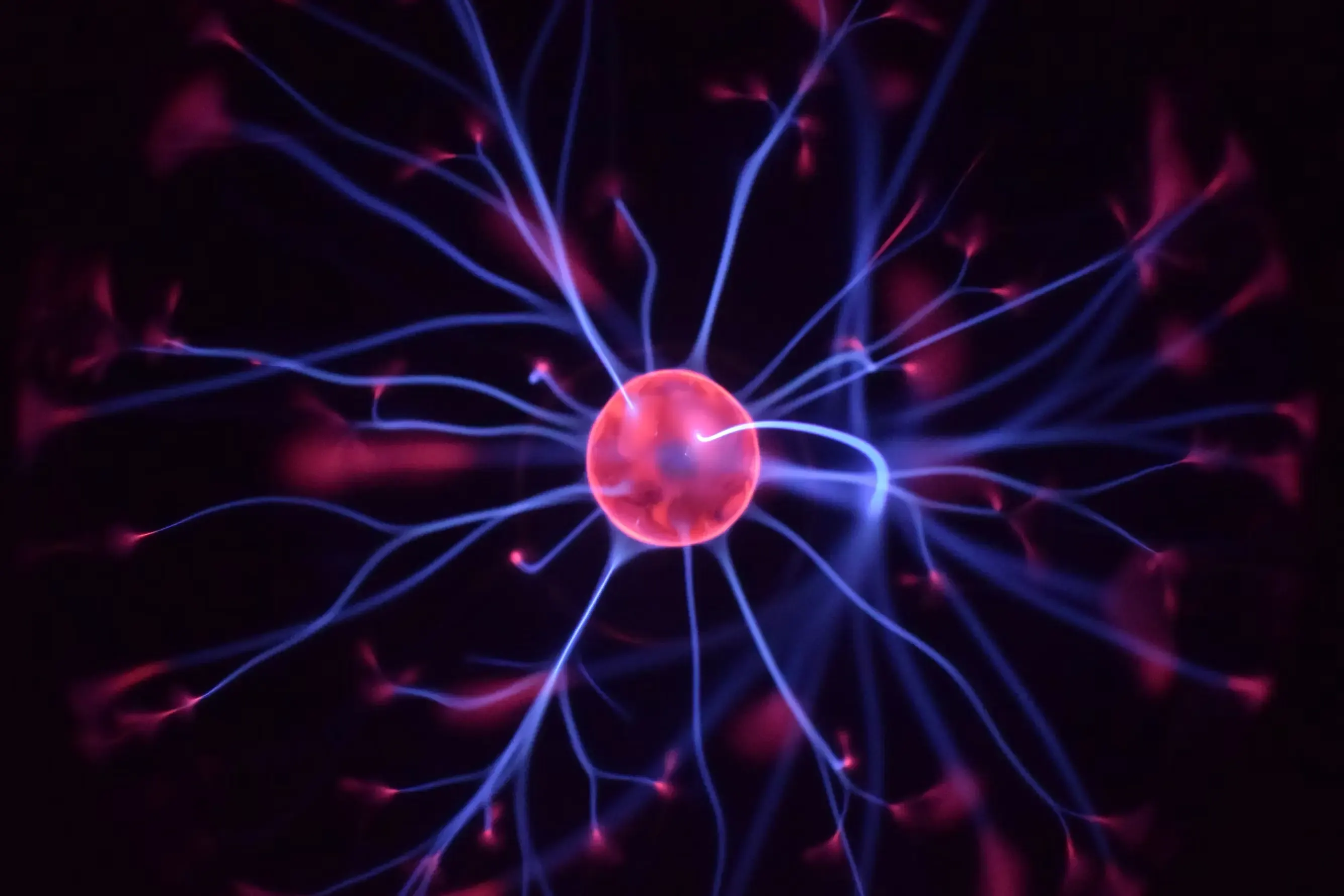 A plasma ball with a glowing red core from which blue electrical filaments radiate against a black background.